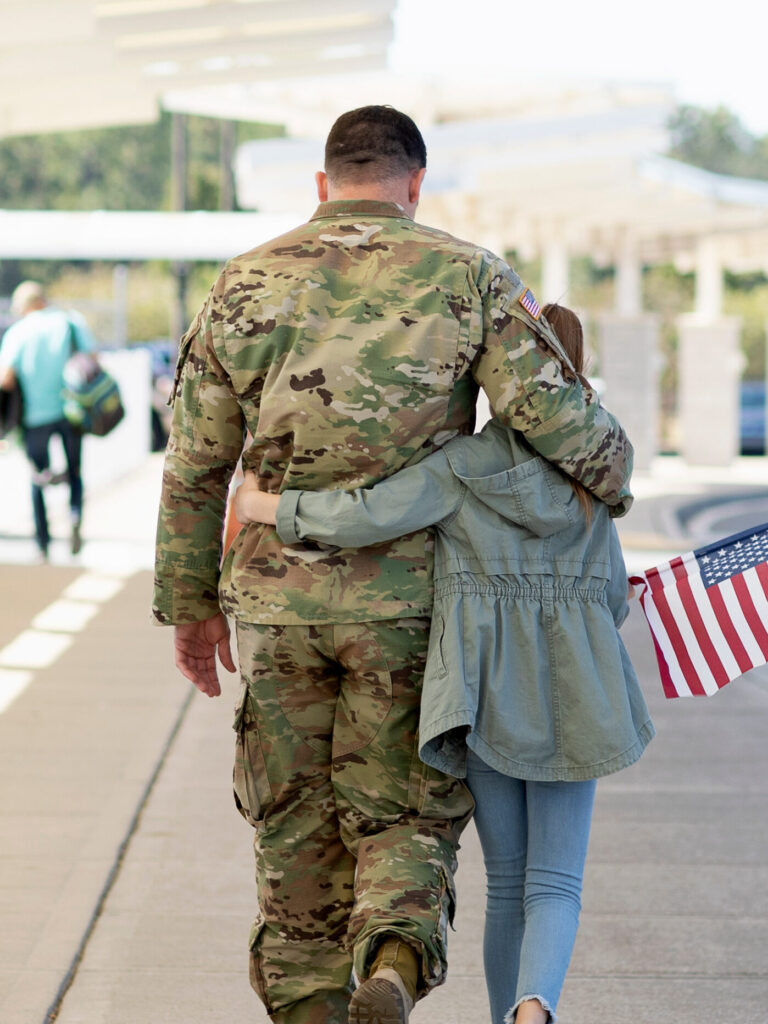 Army soldier walking with his daughter at an airport. Welcoming him home from a deployment and holding an American flag.