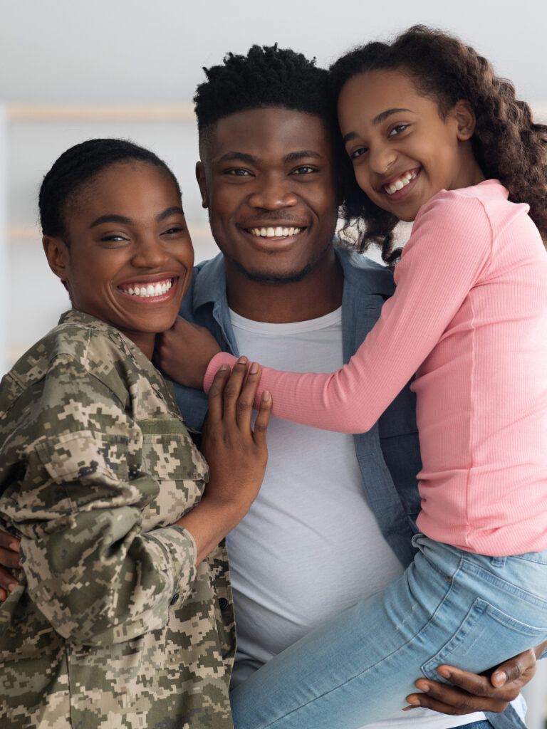 Happy African American woman in military uniform posing with her family at home, female soldier reunited with her husband and daughter, embracing all together and smiling at camera